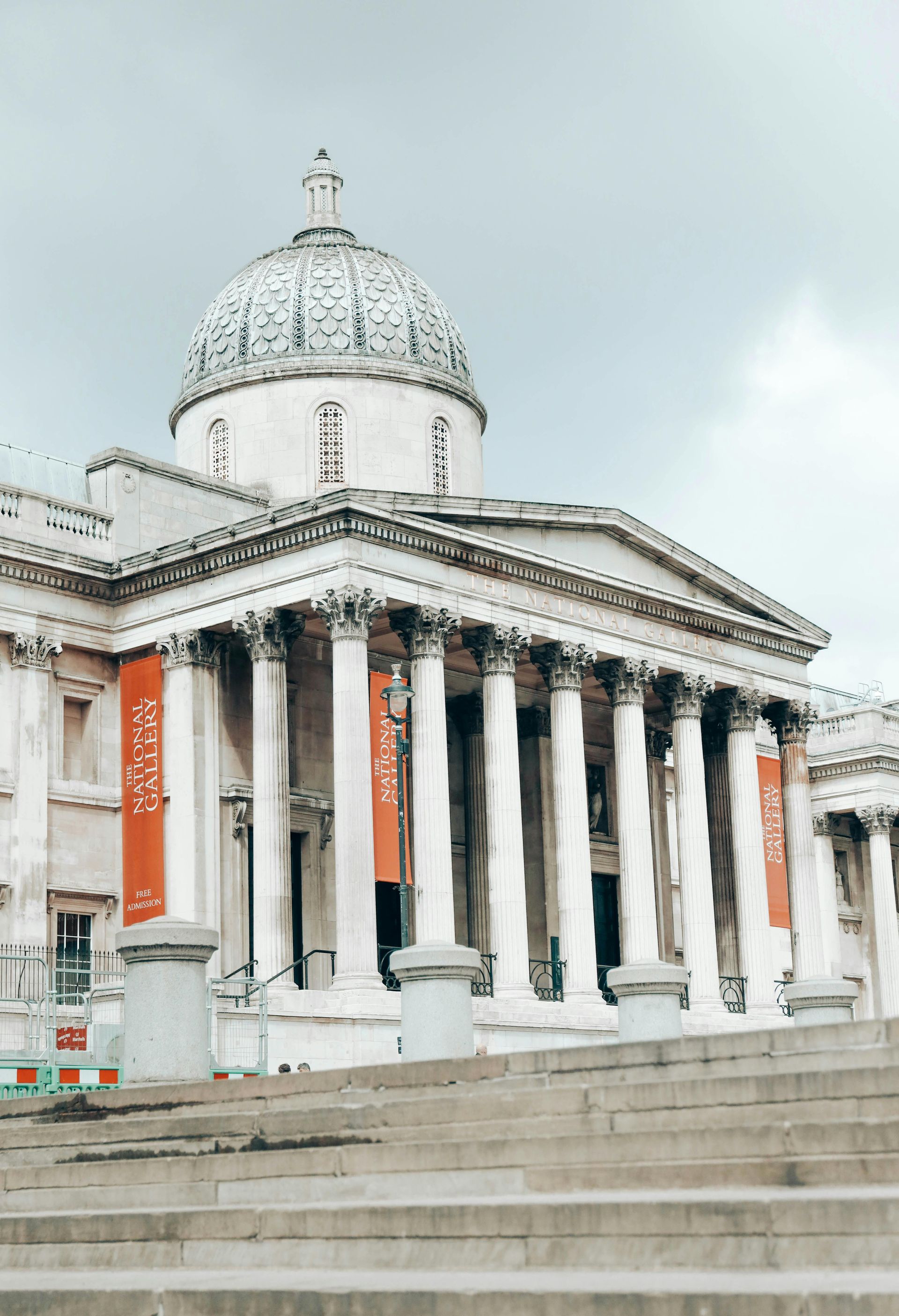 Neoclassical building with a domed roof and columns; red banners hang on the front. Gray sky, outdoor steps.