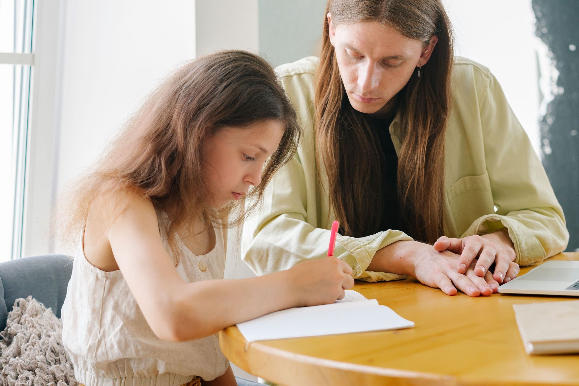 Un adulto aiuta un bambino a scrivere a un tavolo con carta e matita in una stanza luminosa.