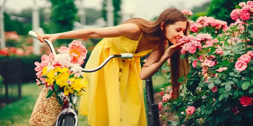 A woman in a yellow dress is riding a bike and smelling flowers.