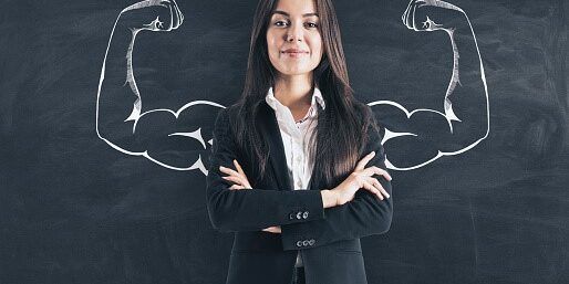 A woman in a suit is standing in front of a blackboard with muscles drawn on it.