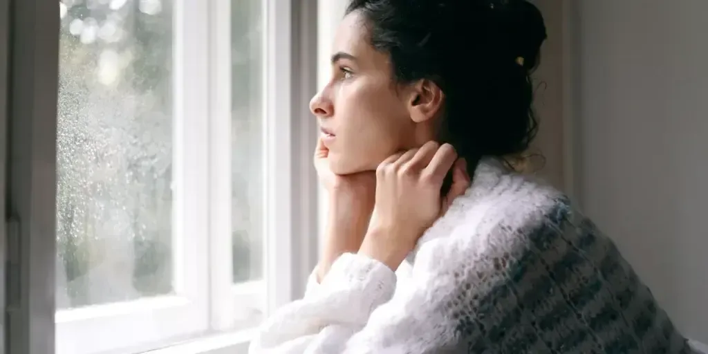 A woman is looking out of a window on a rainy day.
