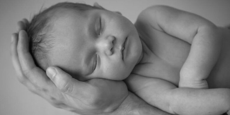 A black and white photo of a baby sleeping in a person 's hands.