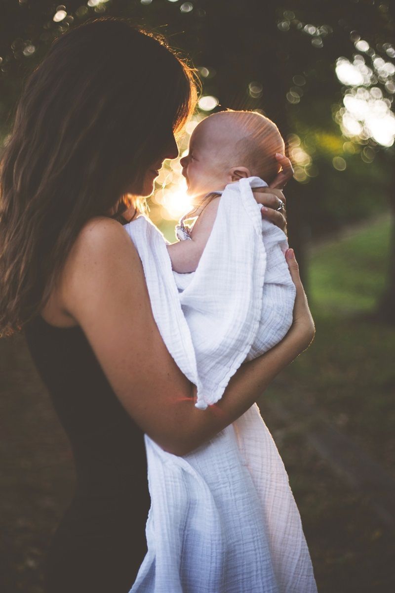A woman is holding a baby wrapped in a white blanket.
