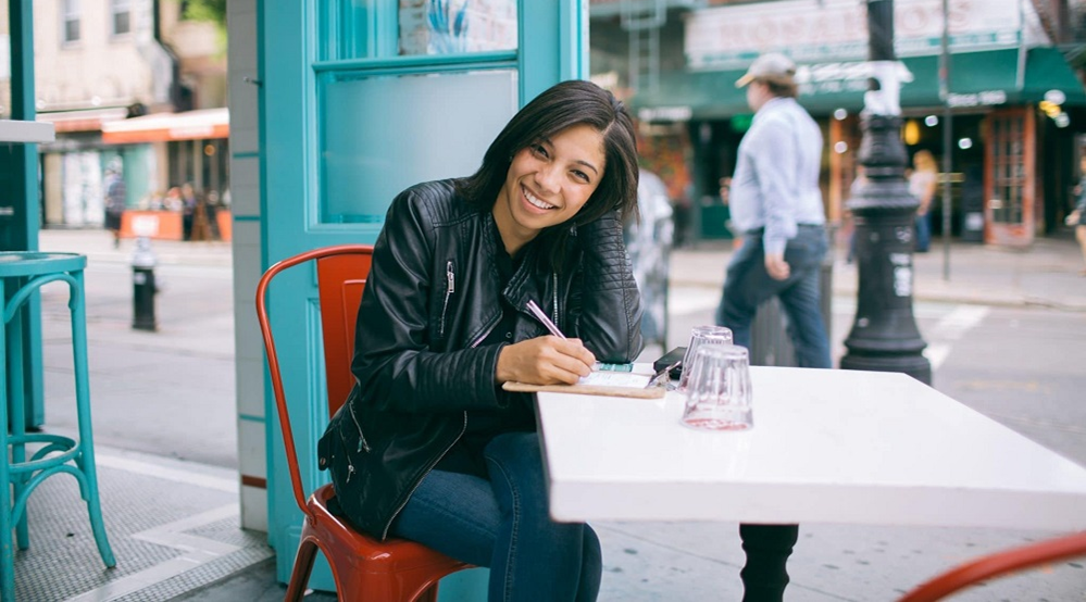 A woman is sitting at a table writing in a notebook.