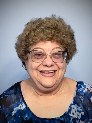 A woman wearing glasses and a blue shirt is smiling for the camera.