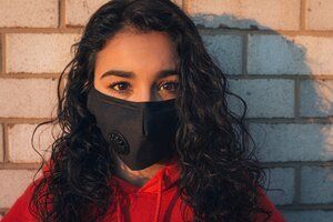 A woman wearing a black face mask is standing in front of a brick wall.