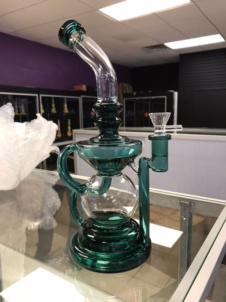 A green glass bong is sitting on top of a glass table