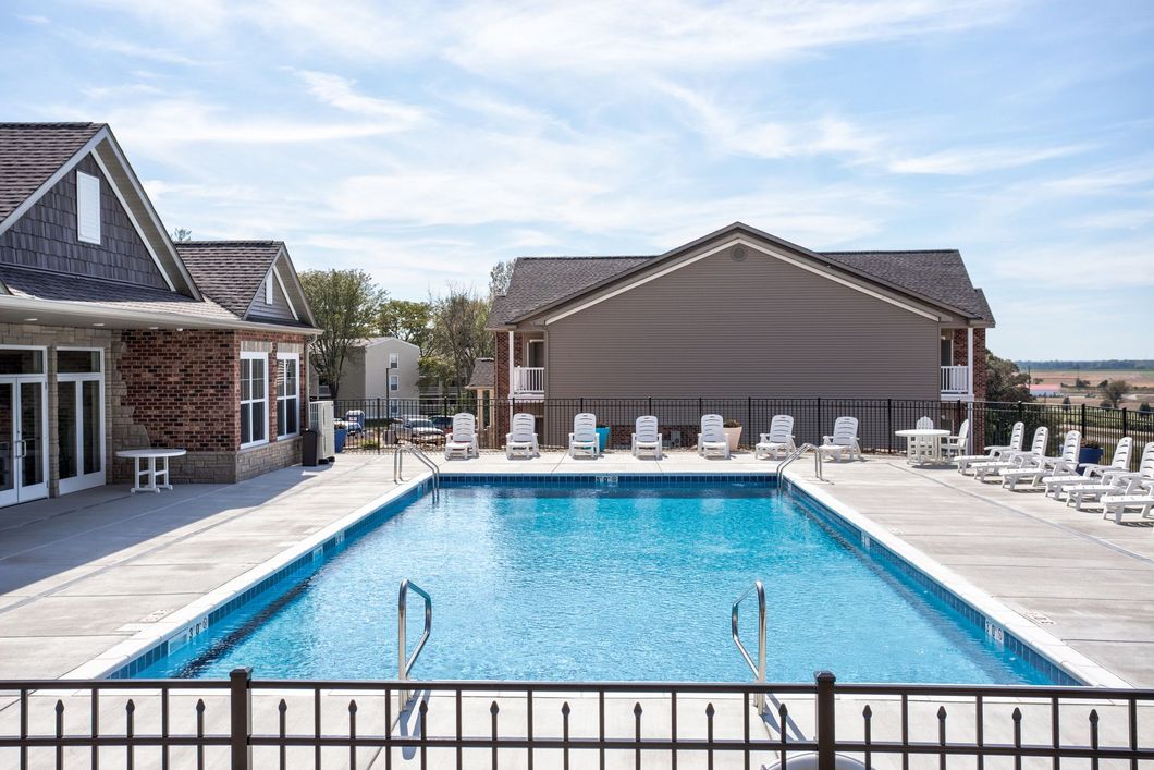 A large swimming pool surrounded by chairs and a fence in front of a building.