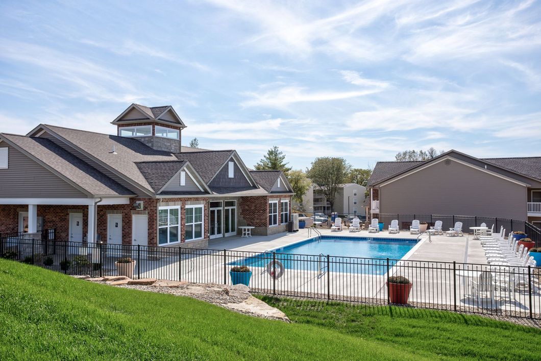A large swimming pool is surrounded by a fence in front of a house.