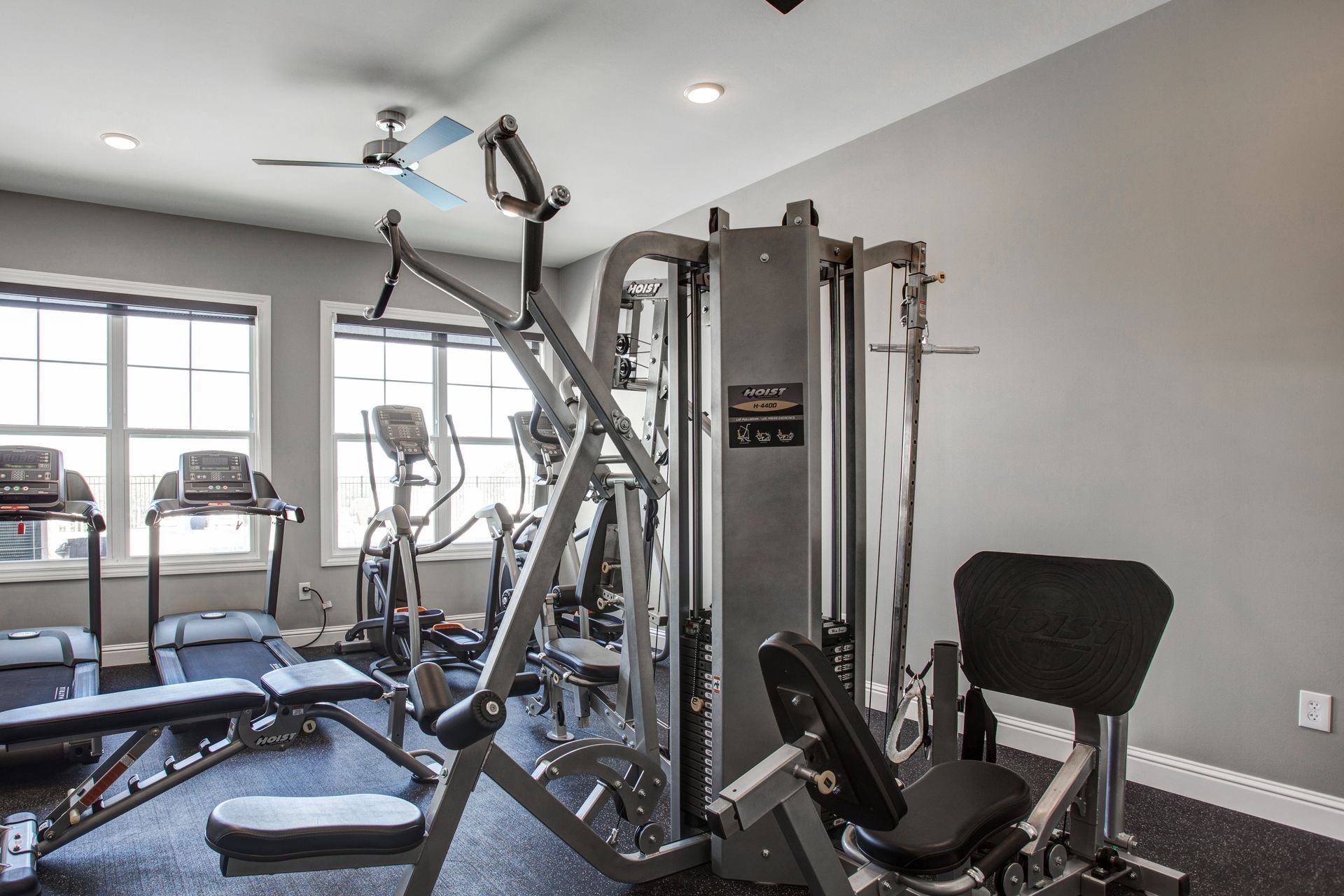 A gym with a lot of exercise equipment and a ceiling fan.