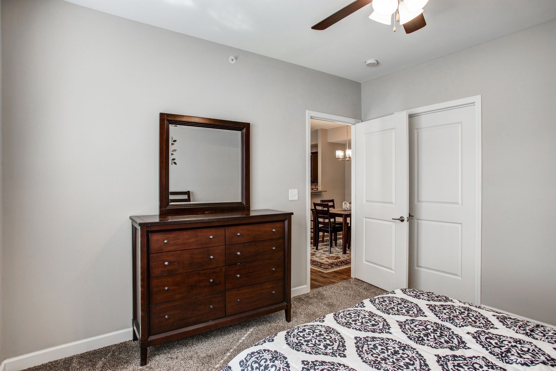 A bedroom with a bed , dresser , mirror and ceiling fan.