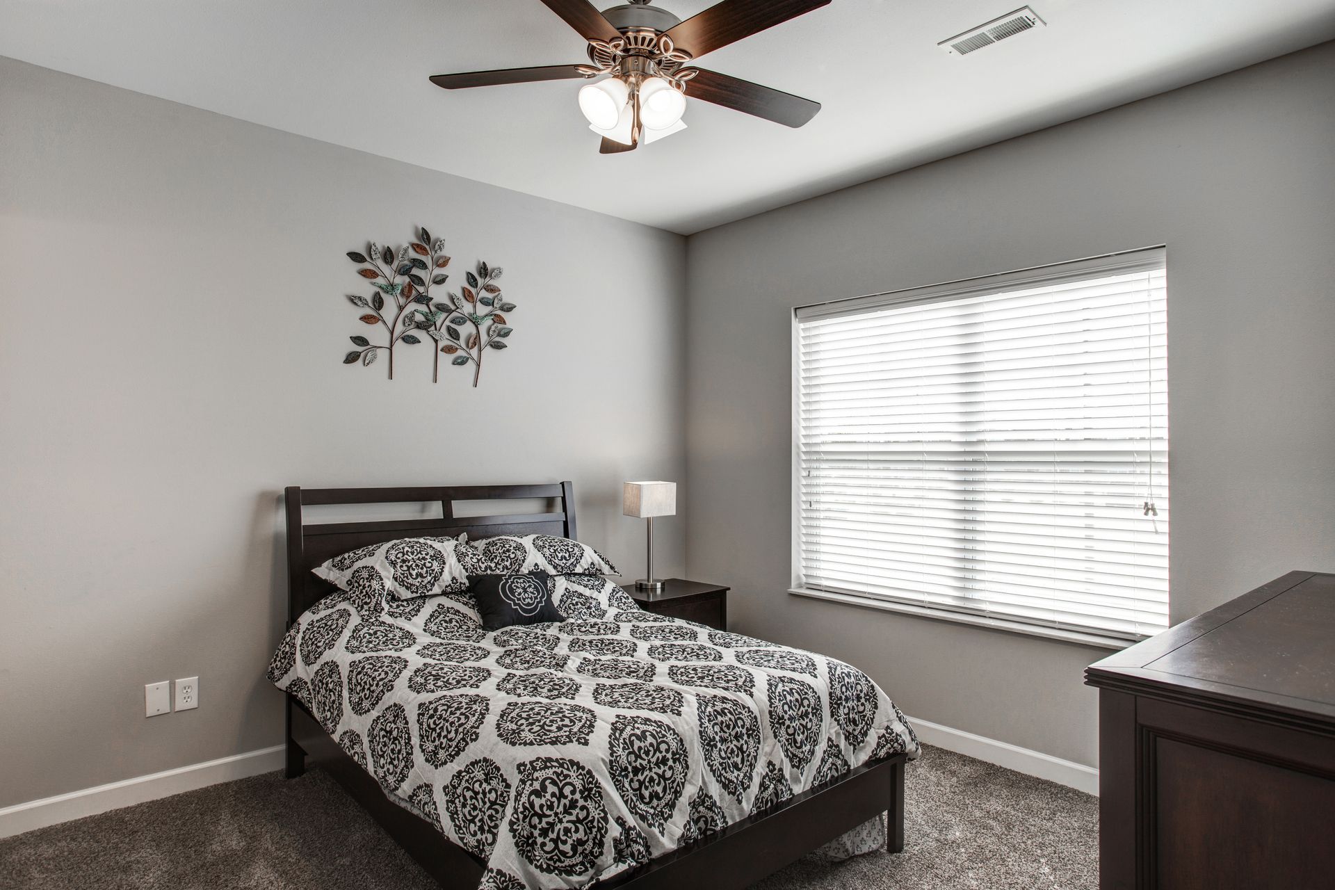A bedroom with a bed , dresser , window and ceiling fan.