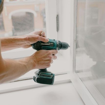 A man is using a drill to fix a window.