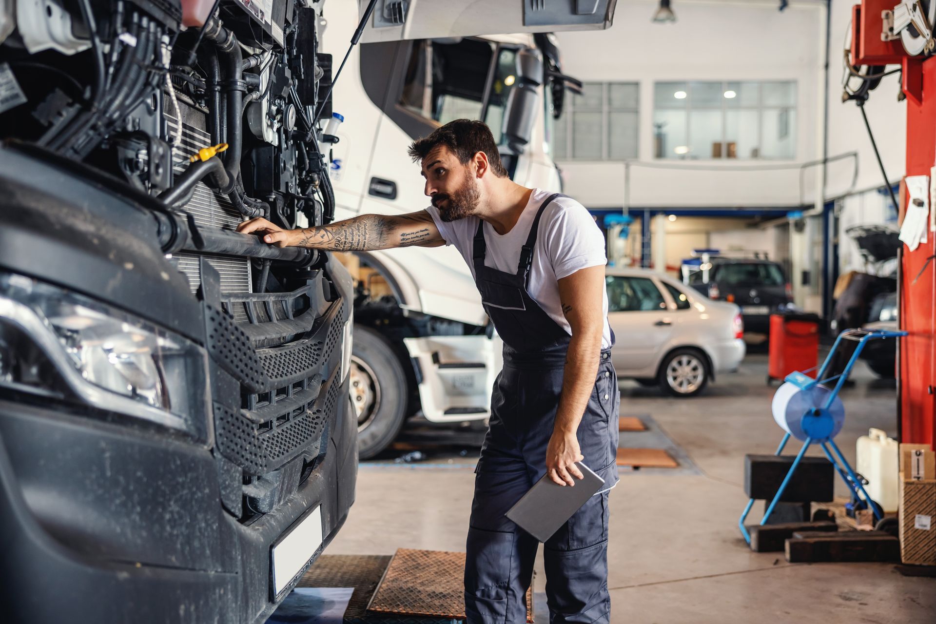 A mechanic is leaning on a truck and checking on a motor while standing in garage