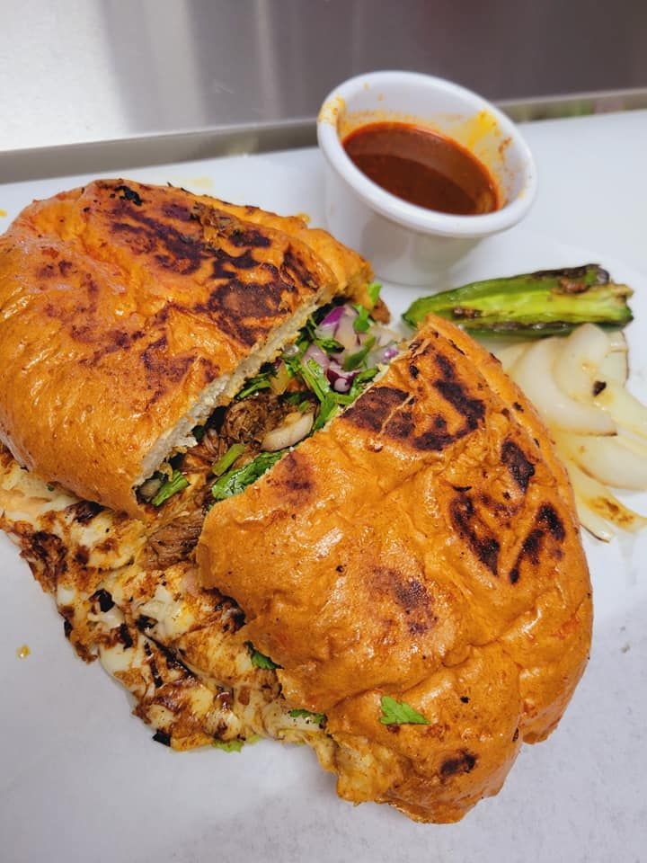 A close up of a sandwich on a plate with a side of sauce.