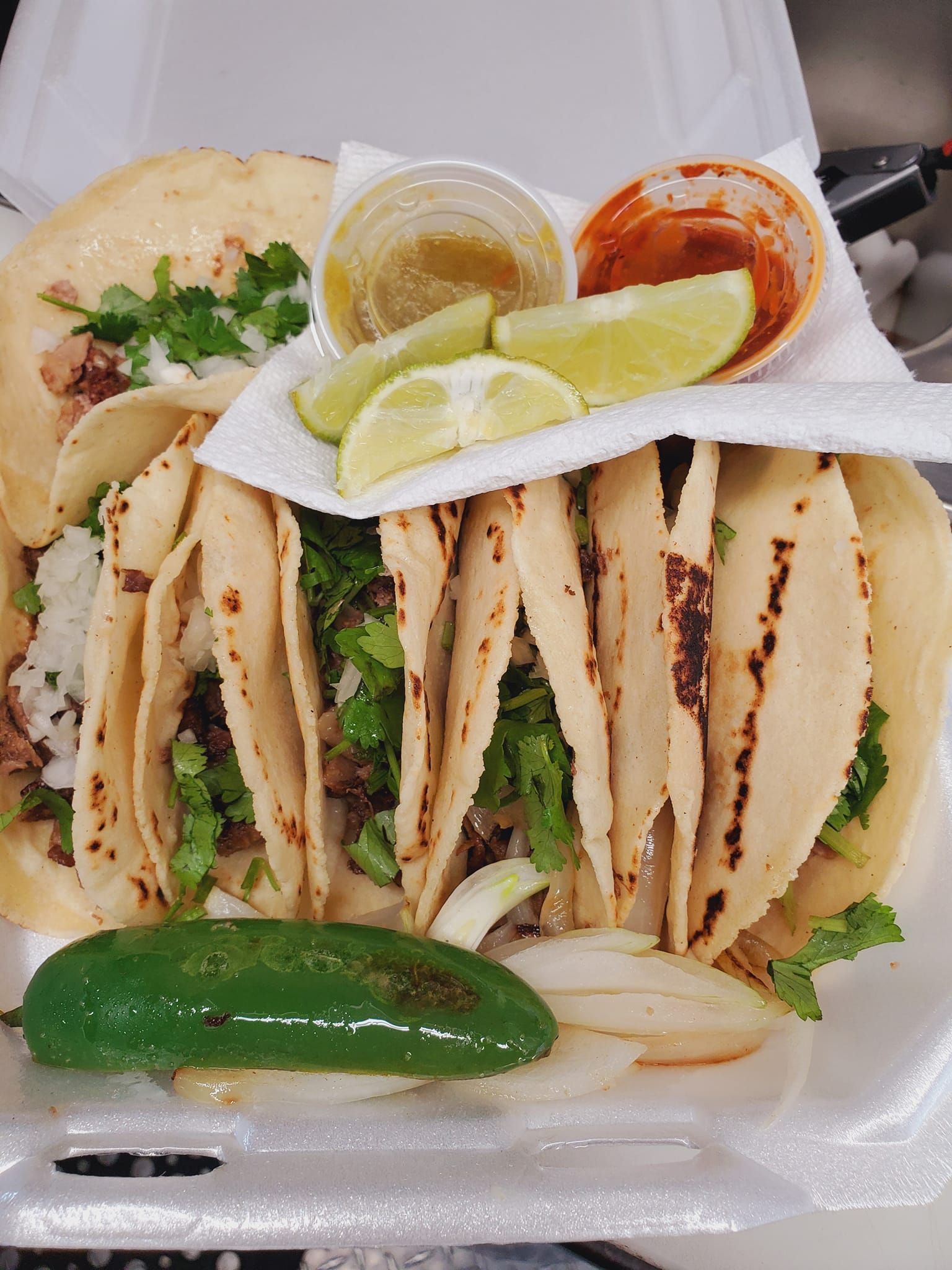 A styrofoam container filled with tacos and sauces.