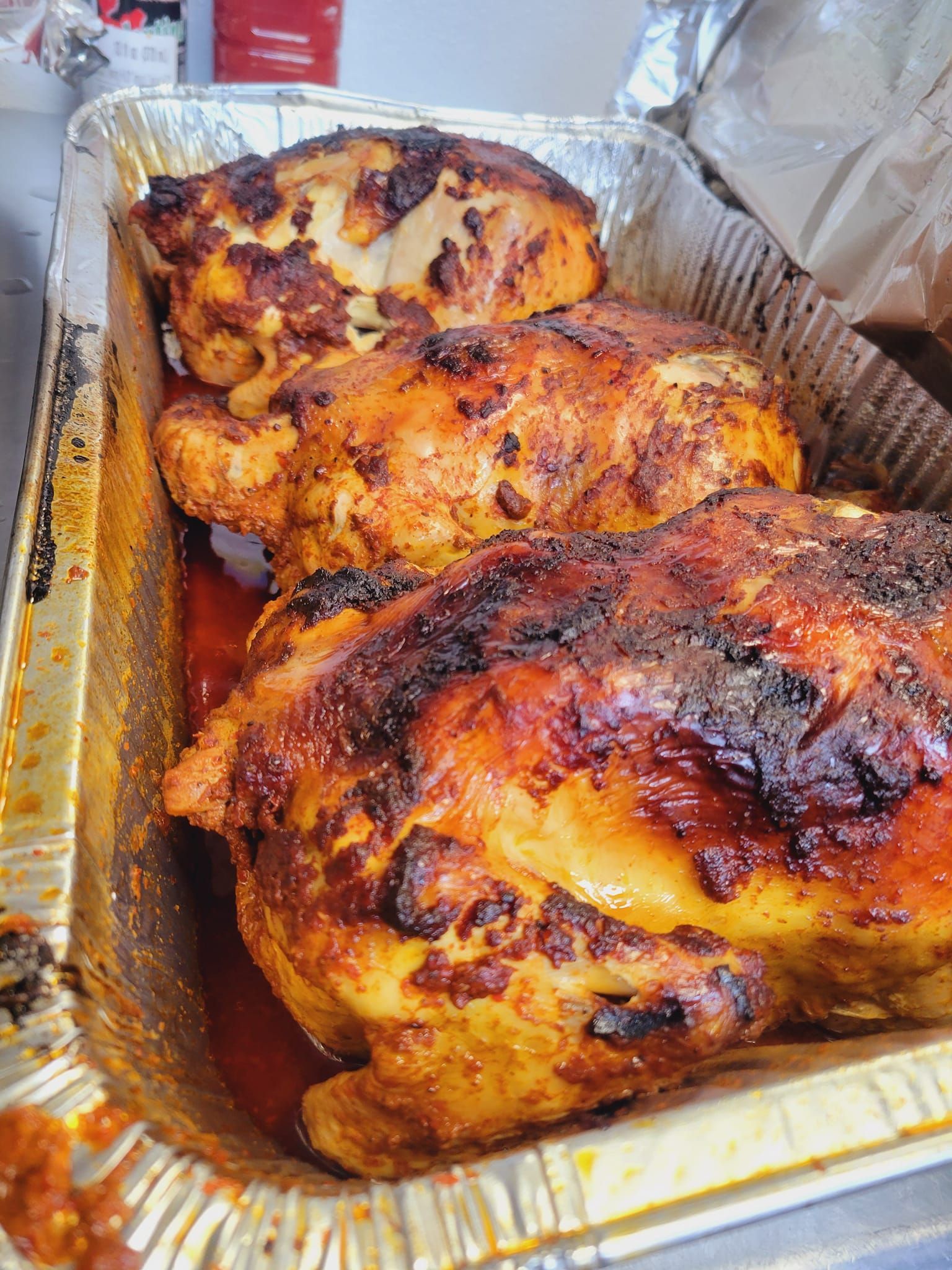 A tin foil pan filled with chicken breasts covered in sauce.