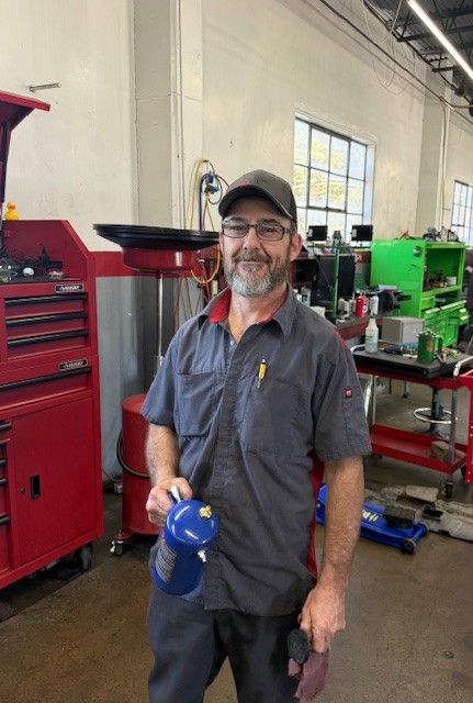 Mechanic in a garage holding a blue bottle, standing beside red tool cabinets and green equipment