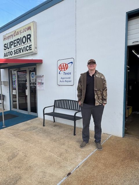 Man standing outside Superior Auto Service beside a bench and AAA sign on a white building