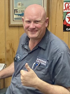 Smiling man in gray work shirt giving a thumbs-up in an office