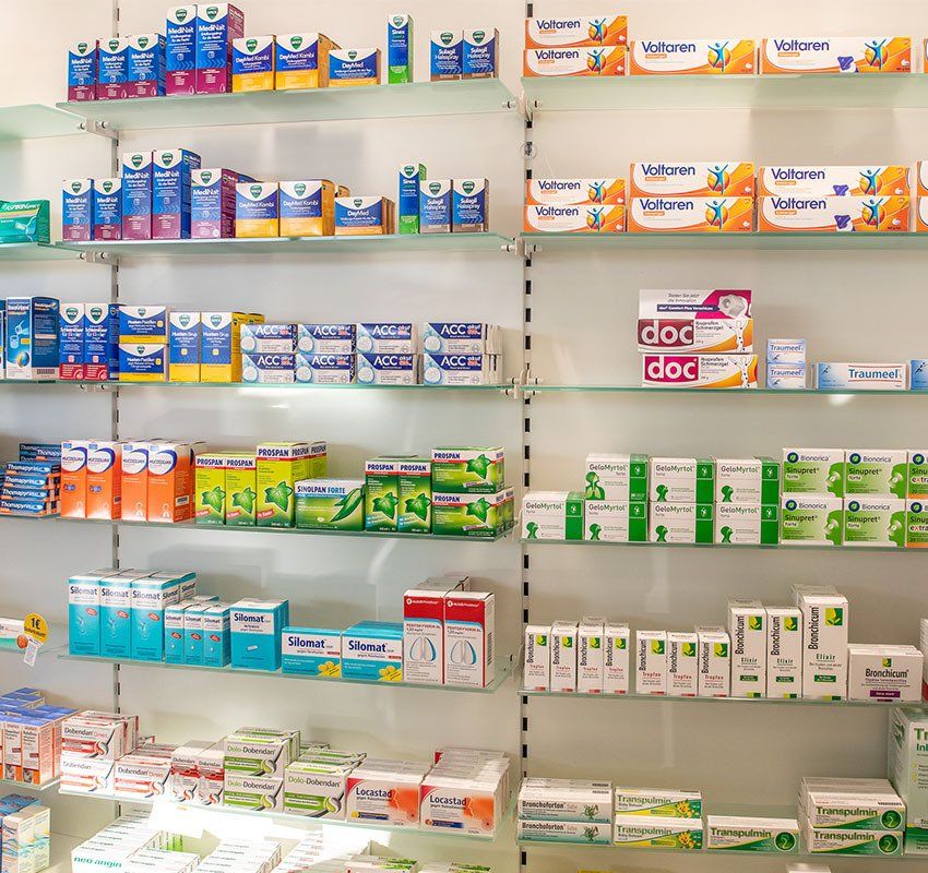 Regale in einer Apotheke, gefüllt mit verschiedenen Medikamentenpackungen, sortiert nach Marke und Art.