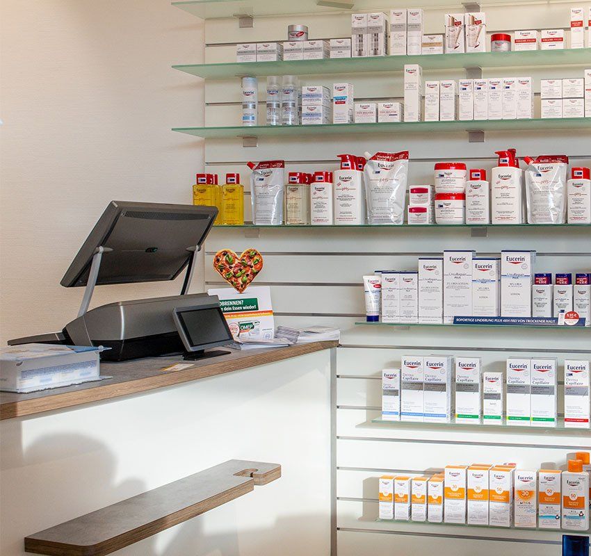 Ein Verkaufstresen mit einer Kasse neben Regalen, die mit verschiedenen Hautpflegeprodukten und Apothekenartikeln gefüllt sind.