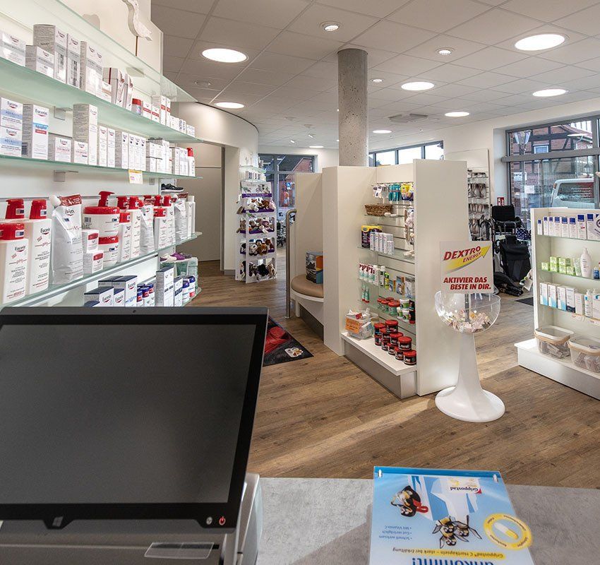 Innenansicht einer Apotheke mit Regalen voller Gesundheitsprodukte, einem Bedienschalter und Produktauslagen.