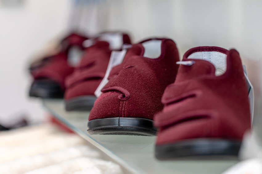 Eine Reihe bordeauxroter, filzartiger medizinischer oder orthopädischer Schuhe mit Klettverschlüssen stand auf einem Glasregal.