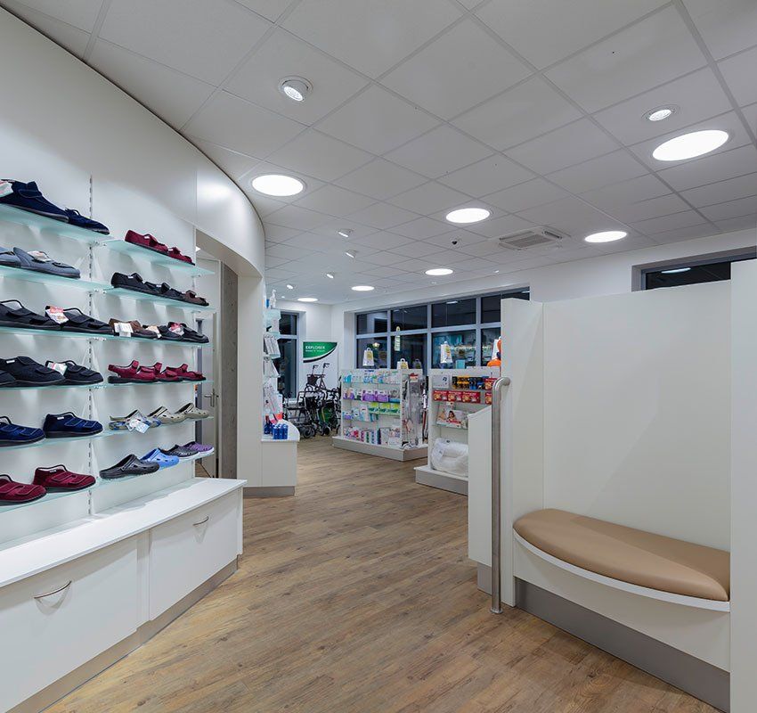Ein helles, modernes Einzelhandelsgeschäft mit Regalen, in denen links verschiedene Schuhe ausgestellt sind, und einer gepolsterten Bank auf der rechten Seite.