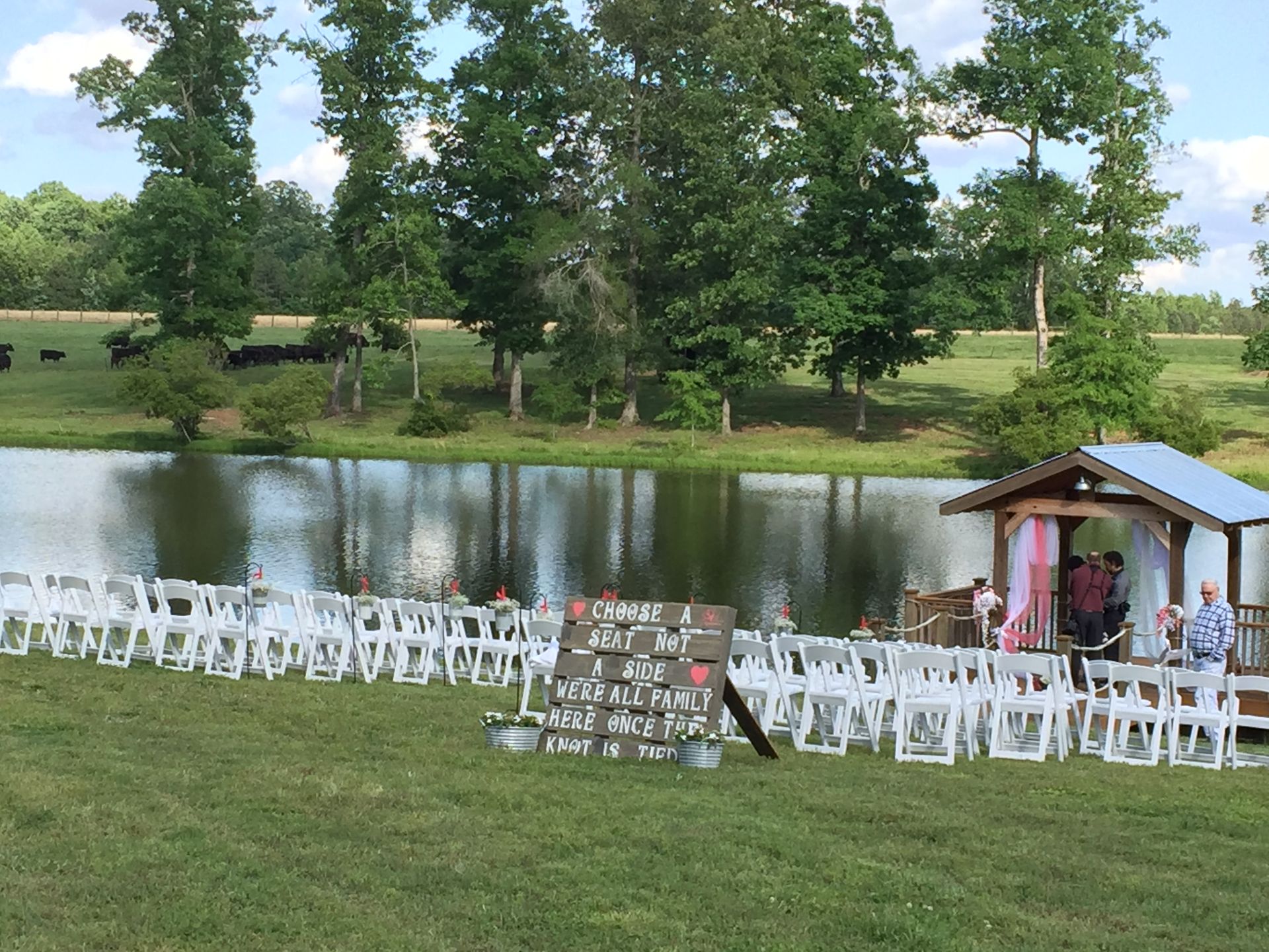 A row of white chairs are lined up in front of a lake.