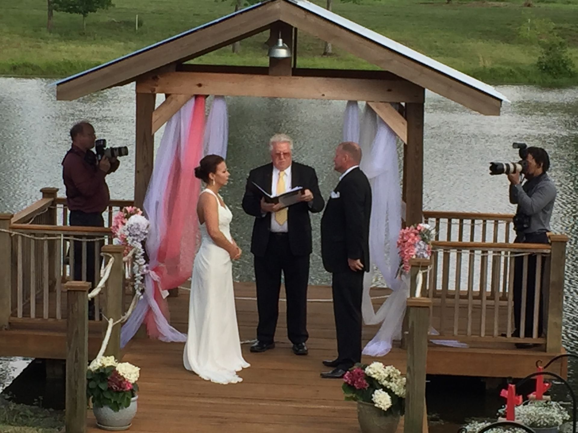 A bride and groom are getting married under a gazebo overlooking a lake.