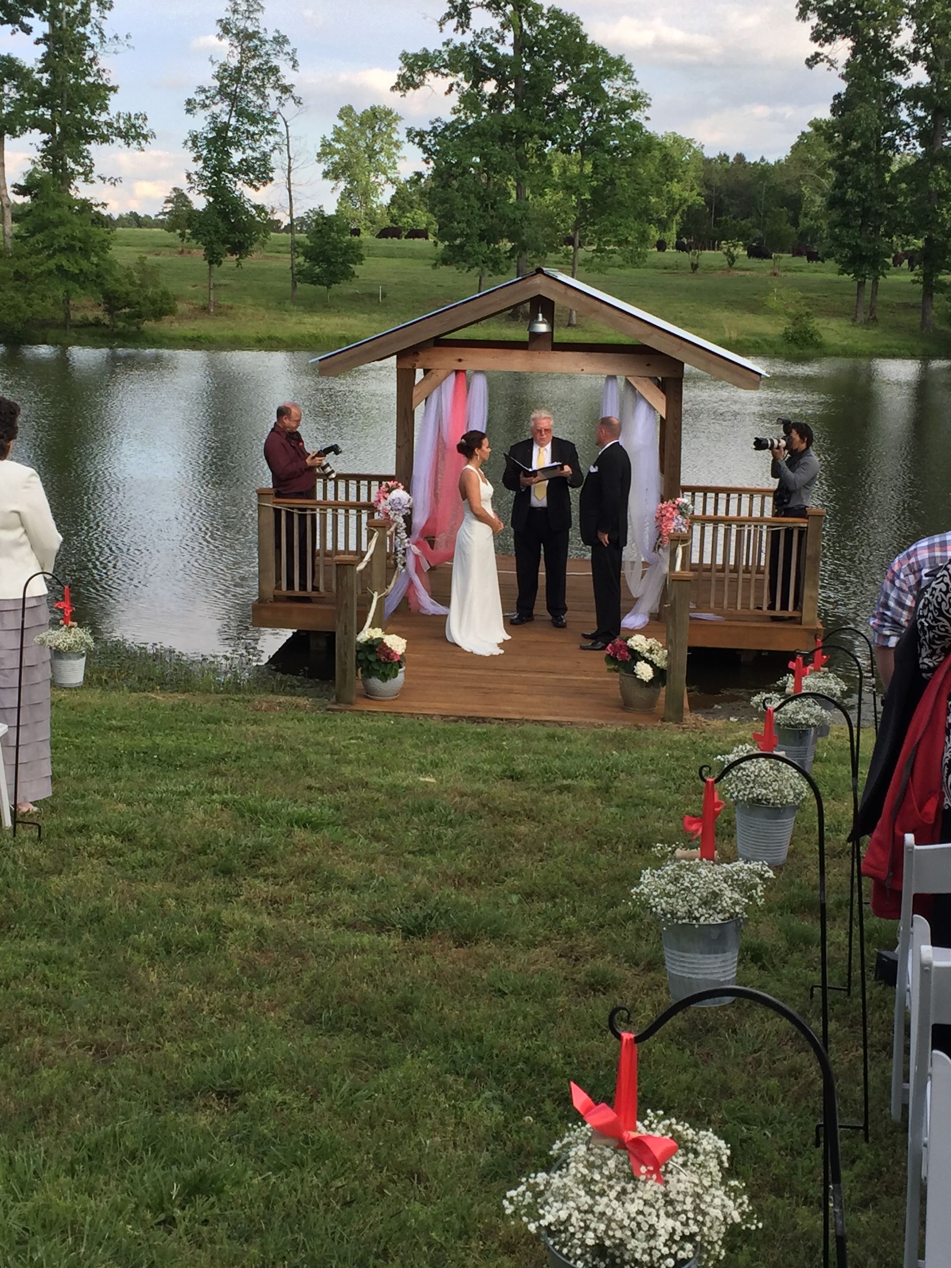 A bride and groom are getting married in a gazebo overlooking a lake