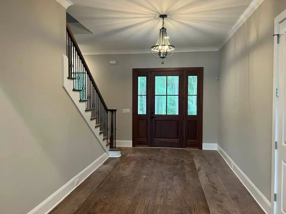 Entryway with wooden door, stairs, and hardwood floor. Light fixture hangs from the ceiling.