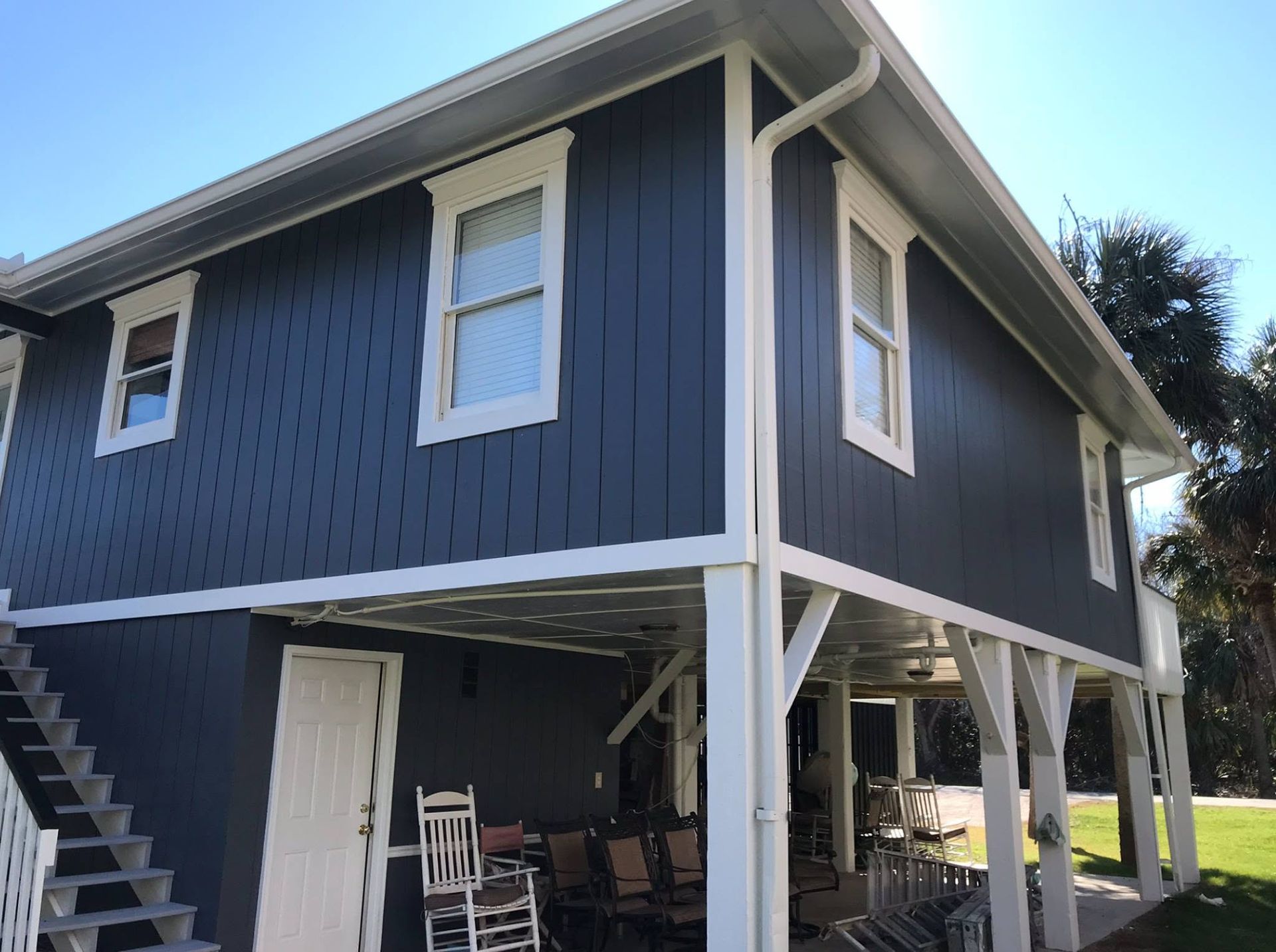 Blue raised house with white trim and stairs, shown from below on a sunny day