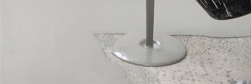A stream of gray liquid being poured onto a rough, light-colored surface.