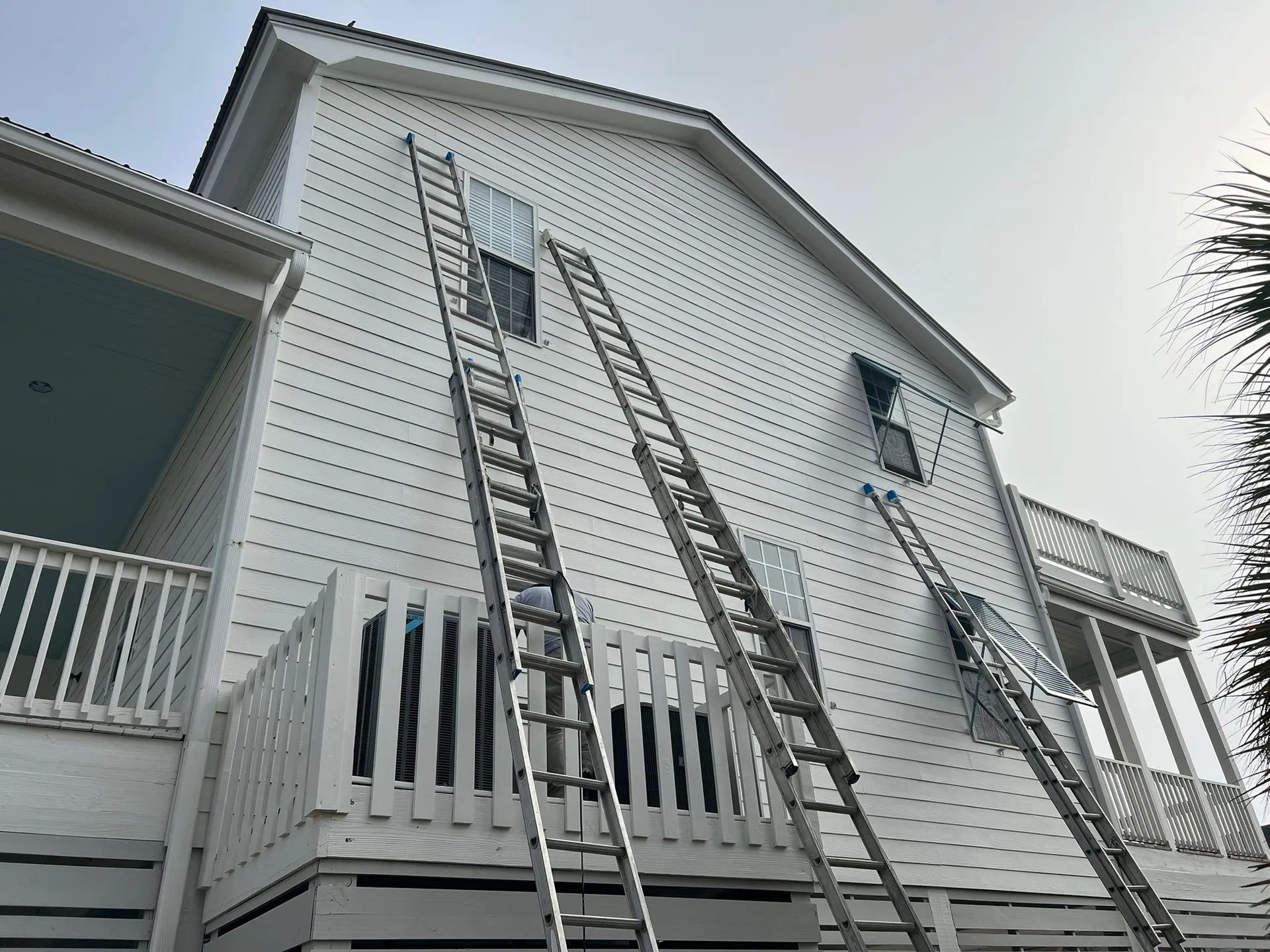 Two ladders leaning against a white house’s upper wall and roofline