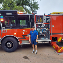 Person in blue stands beside a red fire truck with equipment panels visible.