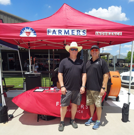 Two people standing at a red FARMERS insurance booth under a canopy outdoors