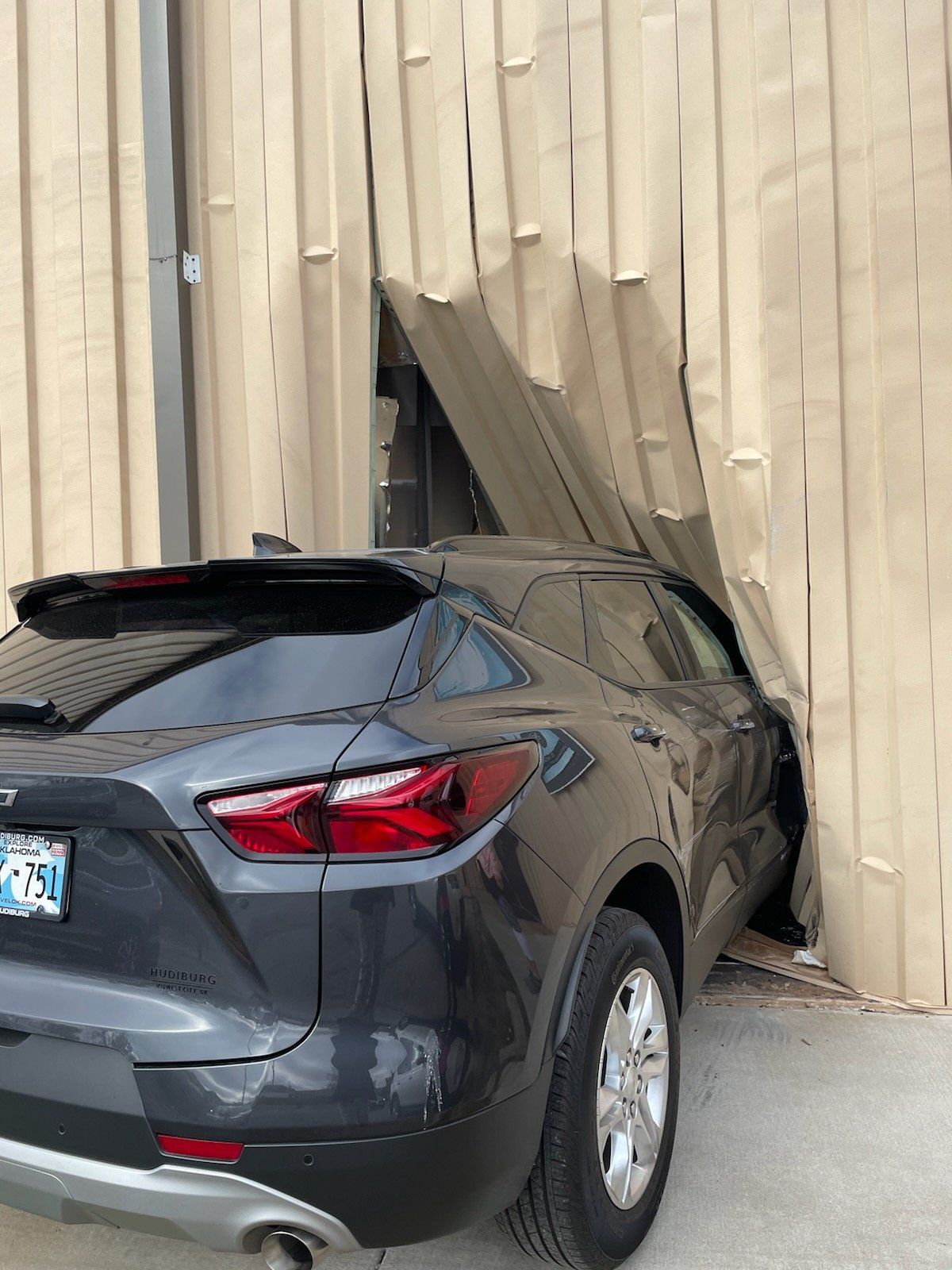 Dark SUV crashed into a tan wall with a large hole in the siding