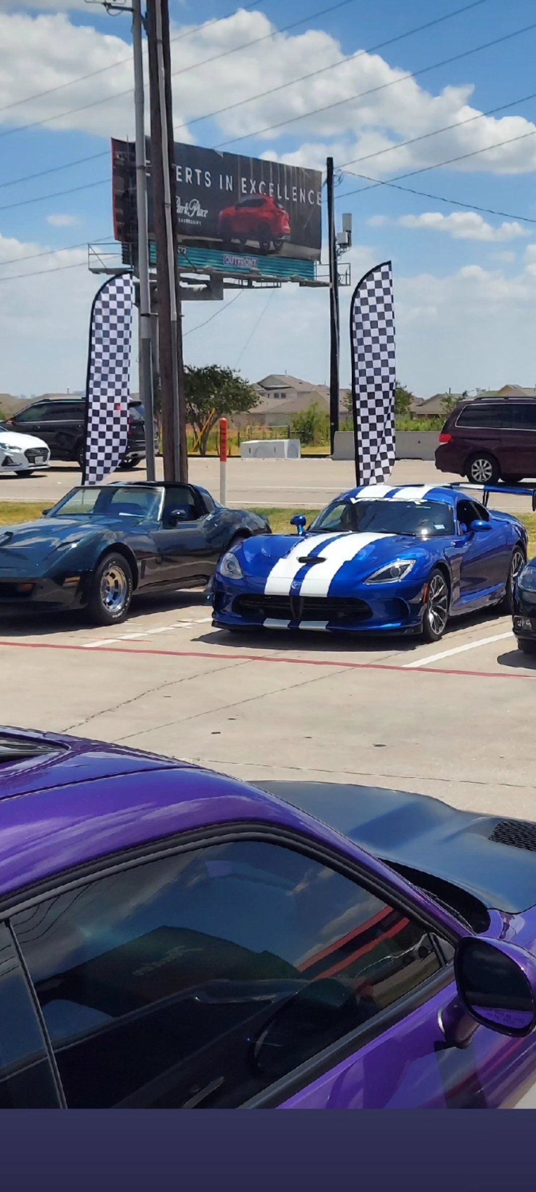 Blue sports cars with white racing stripes on a sunny outdoor lot, with a purple car in the foreground