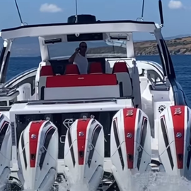 Luxury speedboat on the ocean with four outboard motors and a person standing inside the cabin