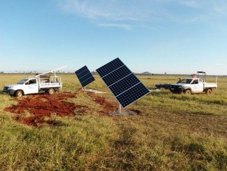 Two trucks are parked in a field next to a solar panel.