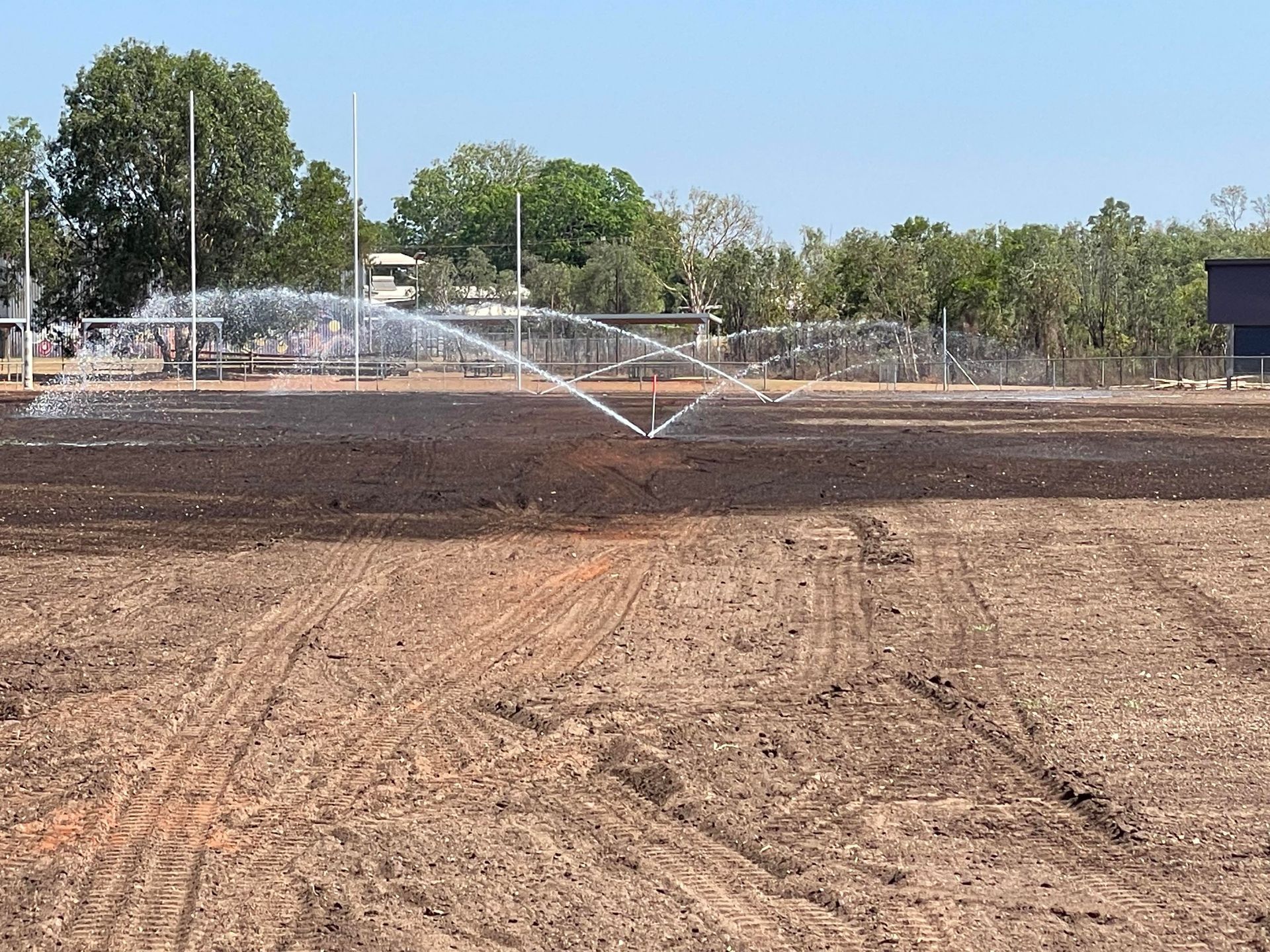 A sprinkler is spraying water on a dirt field.