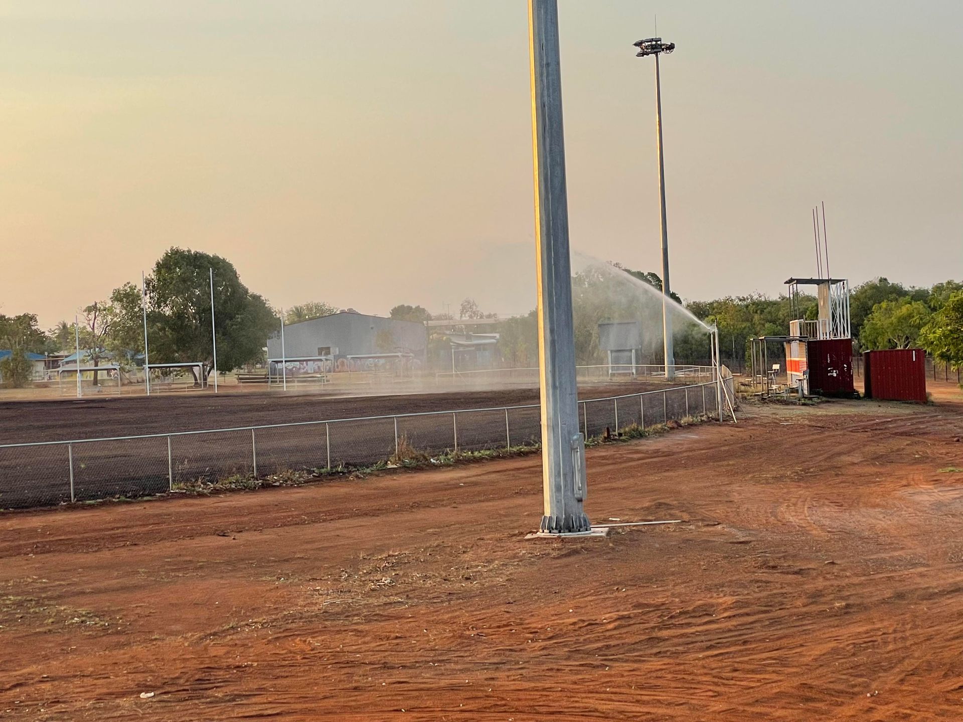A sprinkler is spraying water on a dirt field.