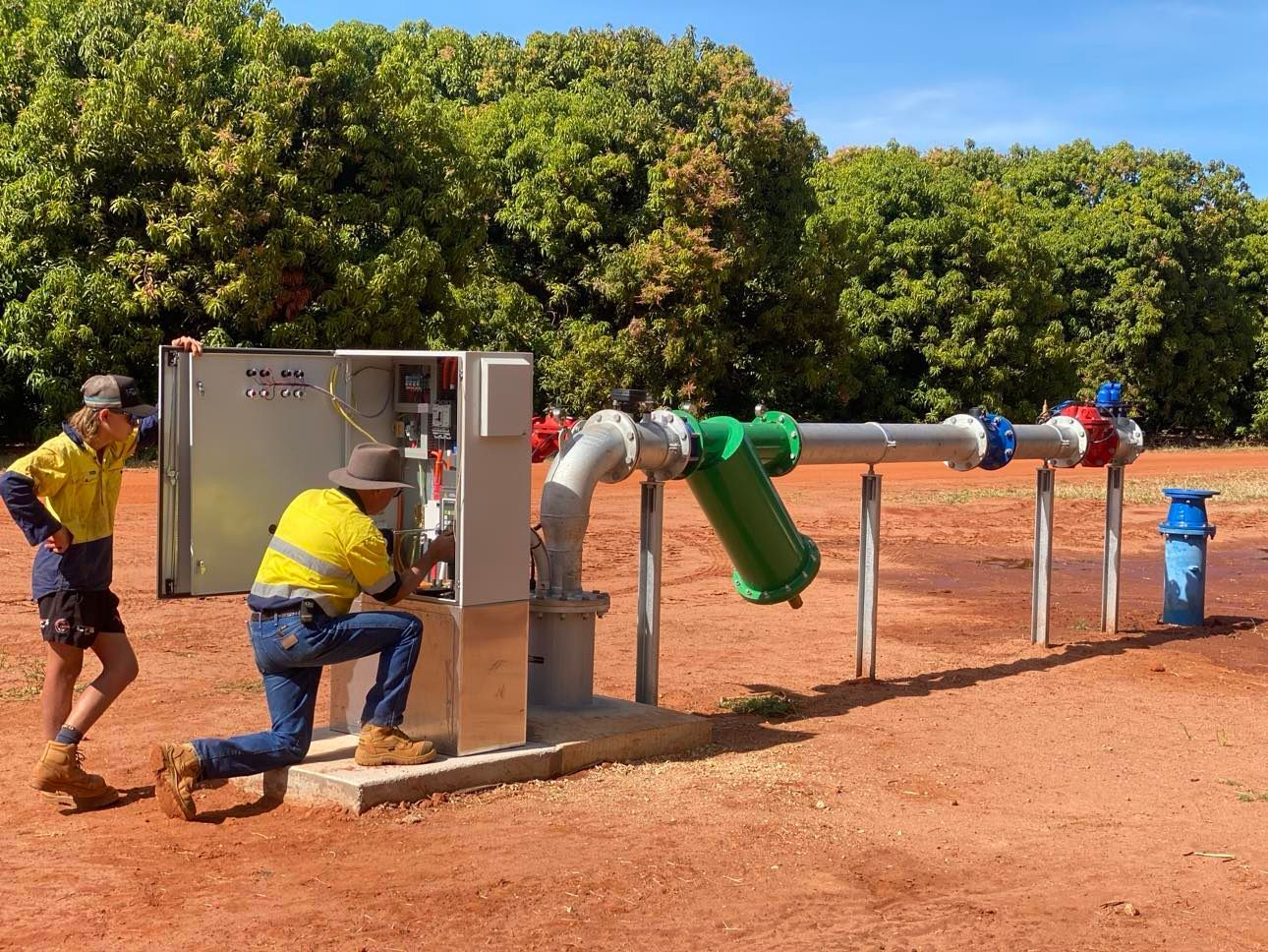 Two men are working on a water pump in a field.