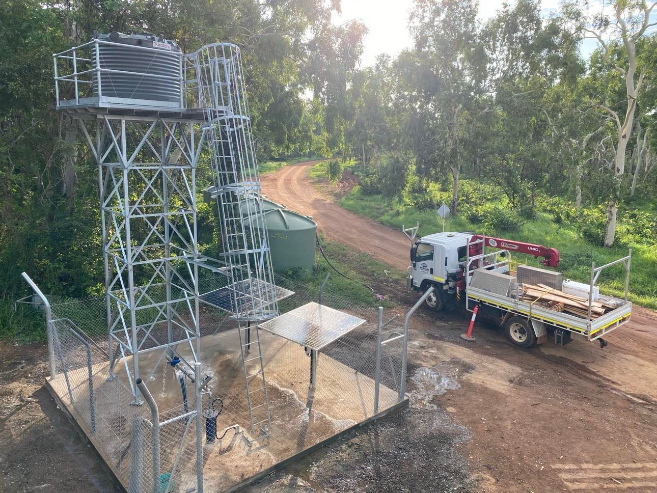 A truck is parked on the side of a dirt road next to a water tower.