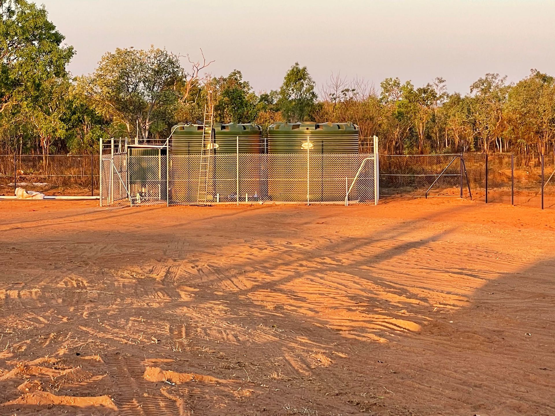A dirt field with a fence and trees in the background