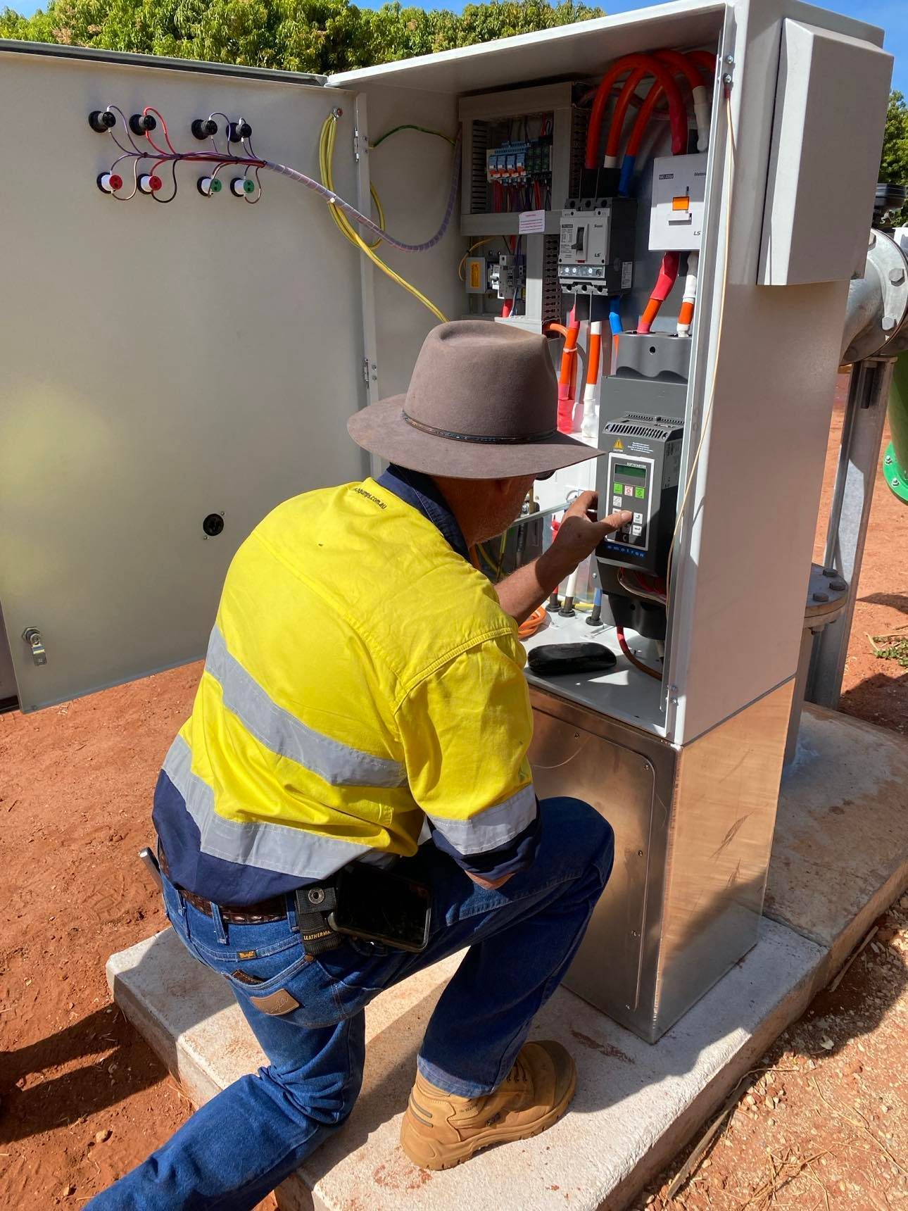 A man in a hat is working on an electrical box.