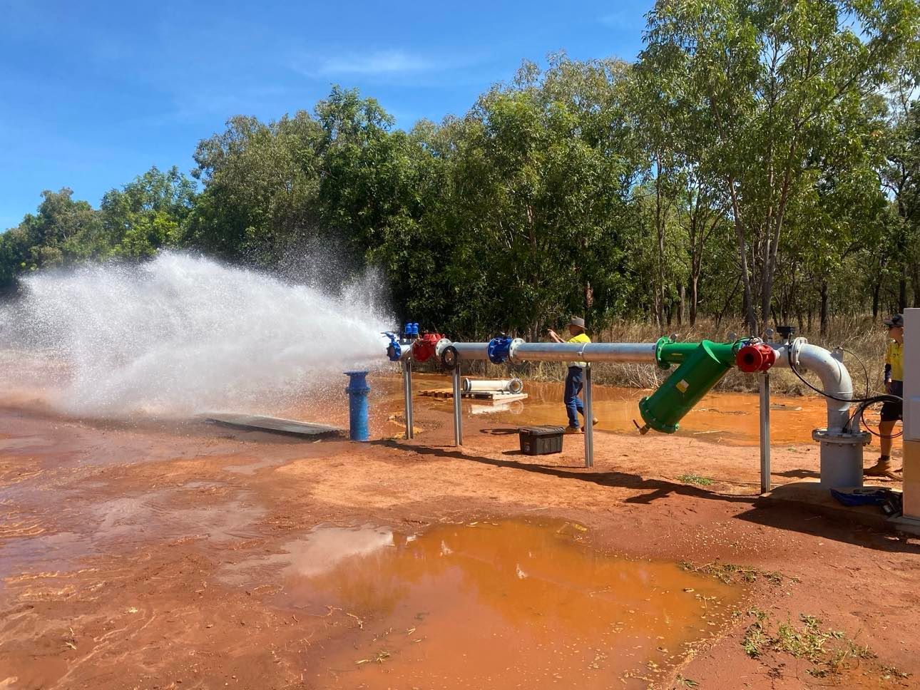A large pipe is spraying water on a dirt field.