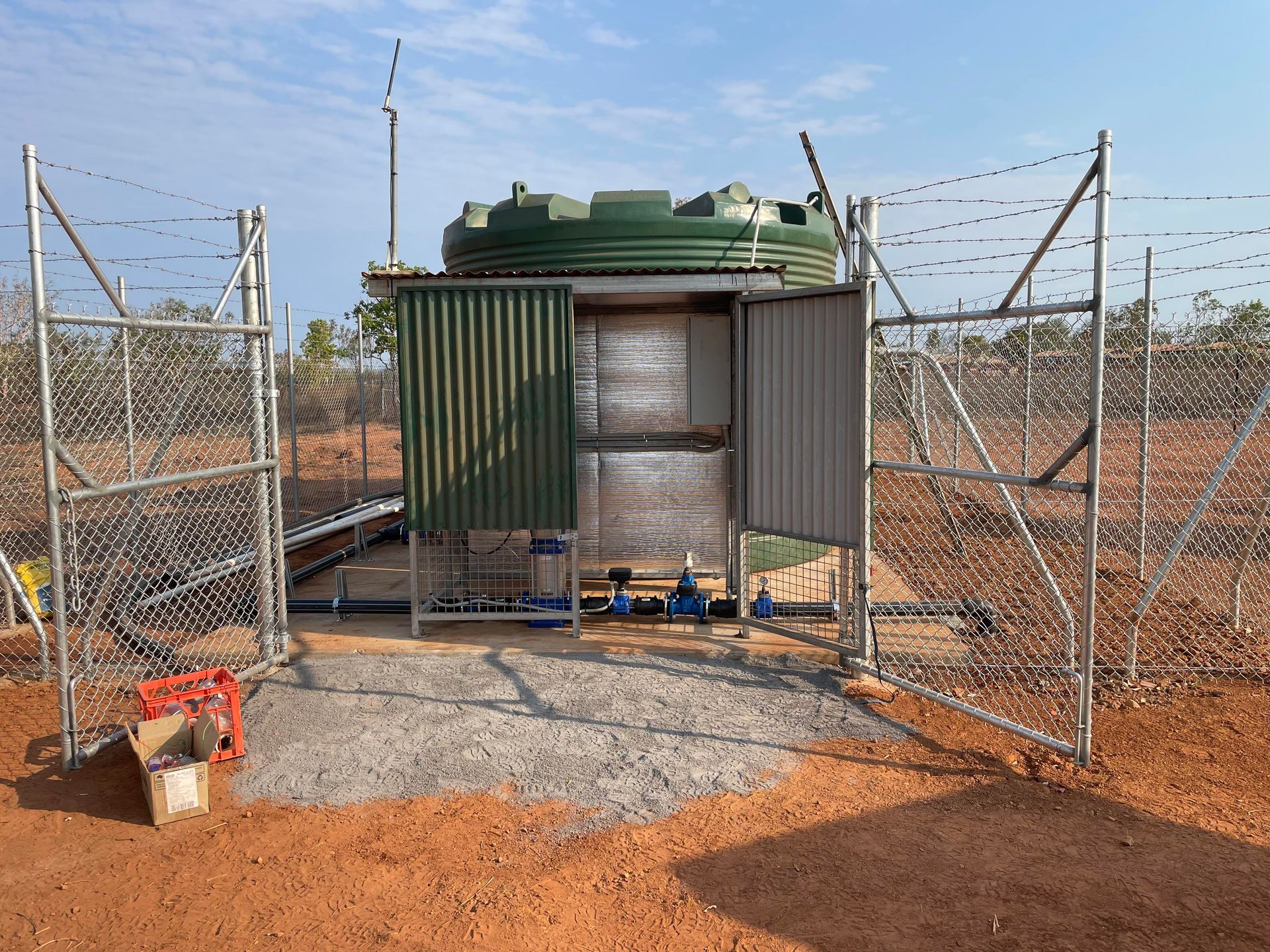 A large green tank is behind a chain link fence.